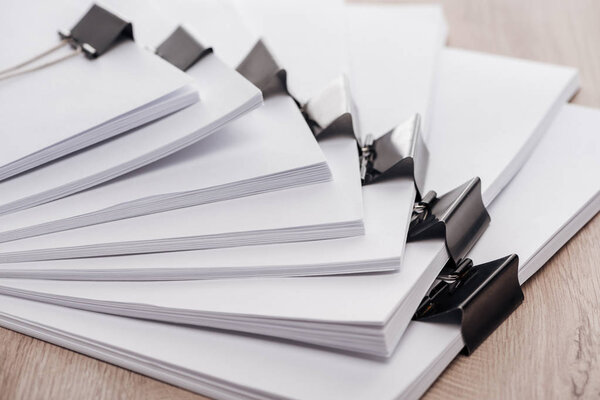 расставлены стопки чистой бумаги с металлическими зажимами на деревянном столе
