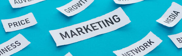 panoramic shot of various components related to marketing on pieces of paper on blue 