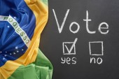 top view of white vote lettering and check mark near yes word on black chalkboard near flag of Brazil