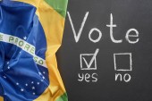 top view of white vote word and check mark near yes word on black chalkboard near flag of Brazil
