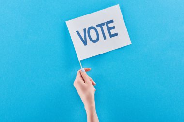 cropped view of woman holding white flag with vote lettering in hand on blue background clipart