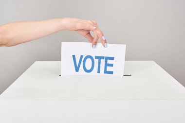 partial view of woman putting card with vote in box isolated on grey clipart