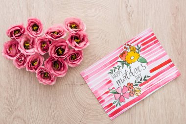 ahşap yüzeyüzerinde mutlu anneler gün yazı ile eustoma çiçek ve kart yapılmış kalp işareti üst görünümü