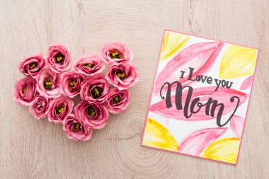 top view of heart sign made of eustoma flowers and card with i love you mom lettering on wooden table clipart
