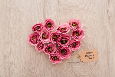 ahşap masa üzerinde mutlu anneler günü kağıt etiket ile eustoma çiçeklerden yapılmış kalp işareti üst görünümü