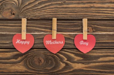 top view of clothes pegs and red paper cards with happy mothers day writing on wooden table clipart