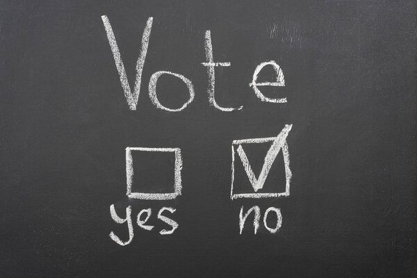 top view of white vote lettering and check mark near no word on black chalkboard