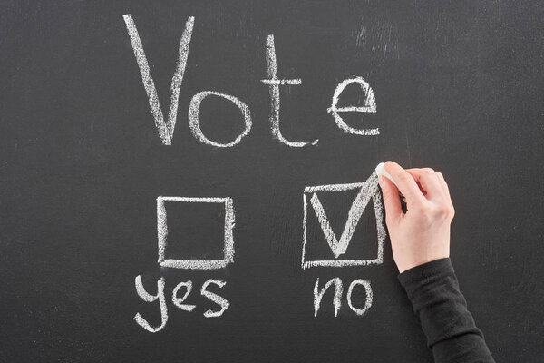 Top view of voter putting check mark near no word on black chalkboard
