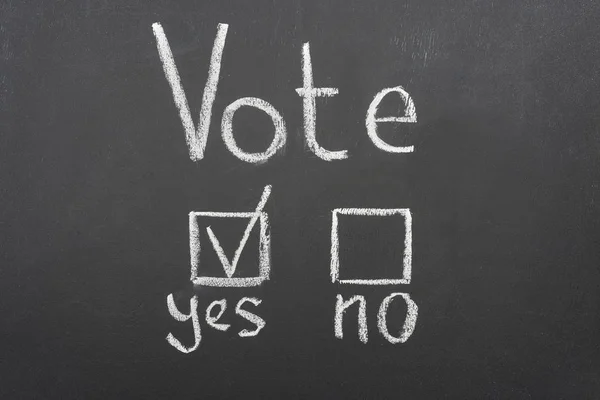 top view of white vote lettering and check mark near yes word on black chalkboard