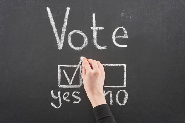 top view of voter putting check mark near yes word on black chalkboard
