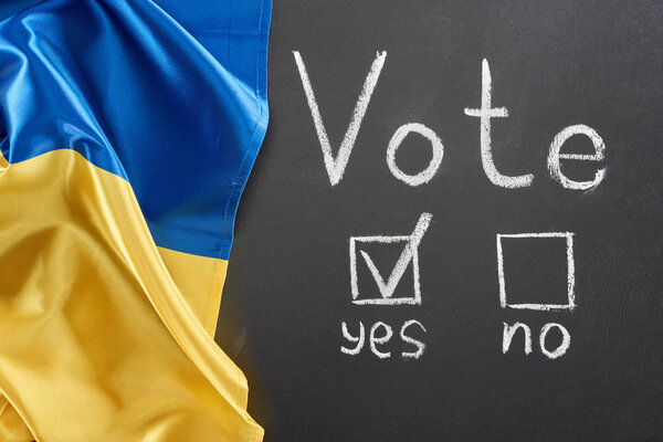 top view of vote lettering and check mark near yes word on black chalkboard near Ukrainian flag