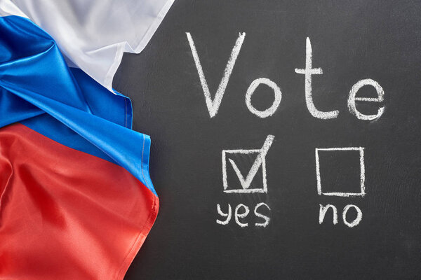 Top view of vote lettering and check mark near yes word on black chalkboard near European flag
