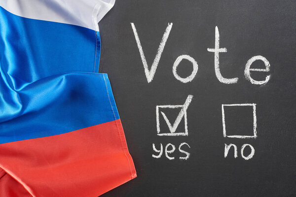 Top view of vote lettering and check mark near yes word on black chalkboard near flag of Russia
