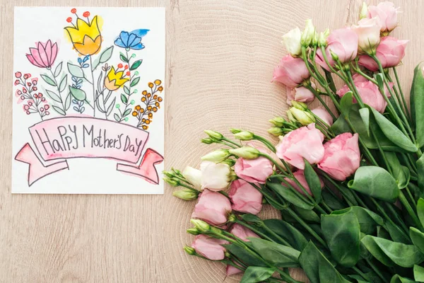 テーブルの上に幸せな母親の日のレタリングとエウストマの花とカードのトップビュー — ストック写真