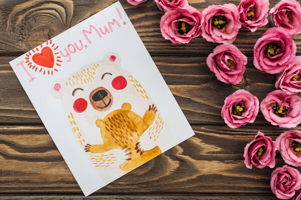 top view of pink eustoma flowers and card with i love you mum lettering on wooden table