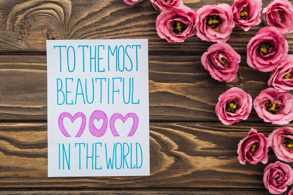 top view of eustoma flowers and card with to the most beautiful mom in the world lettering on wooden table