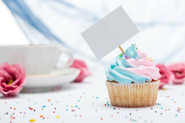 selective focus of delicious cupcake decorated with sprinkles and blank card