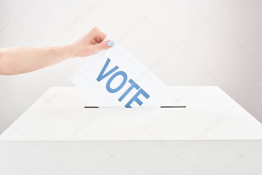 partial view of woman putting vote in box on grey background