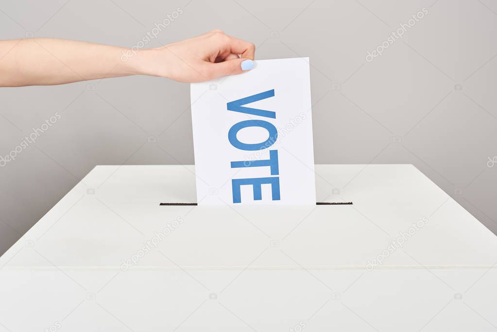 cropped view of woman putting card with vote in box isolated on grey