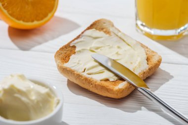 selective focus of toast with butter near knife and half of orange on white  clipart