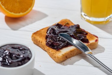 selective focus of toast with jam near knife and half of orange on white  clipart