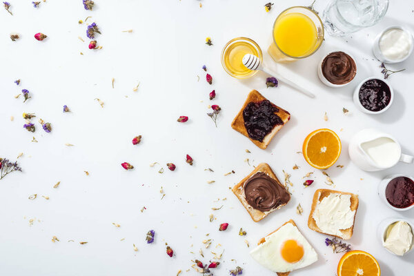 top view of toasts, jam and fried egg near glasses of water and orange juice on white