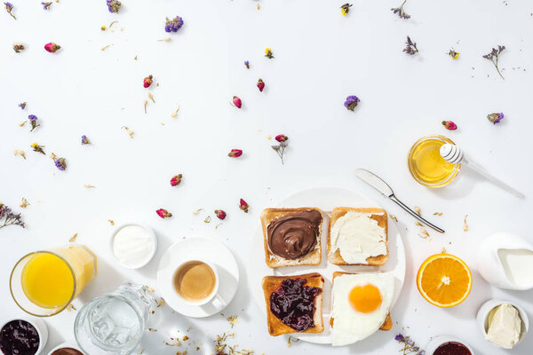 top view of tasty breakfast with toasts and jam near glasses of water and orange juice on white