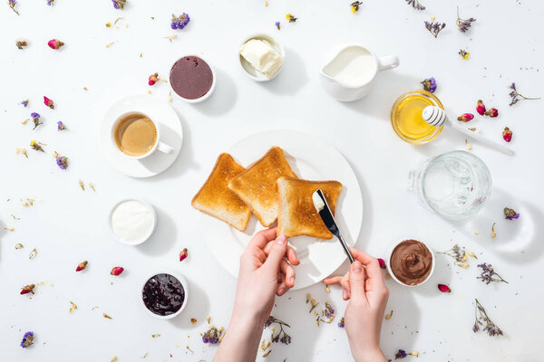 cropped view of woman holding knife near tasty toasts on white 