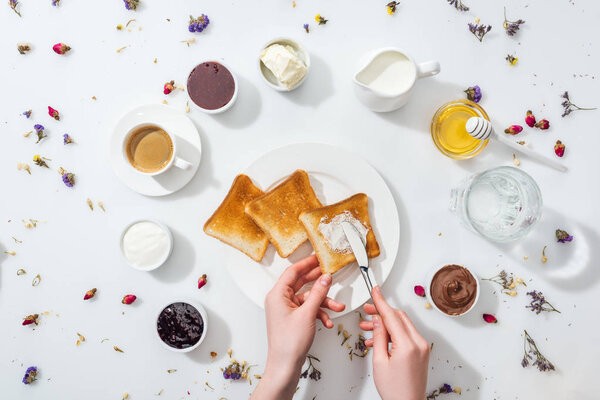 cropped view of woman holding knife near plate with tasty toasts on white 