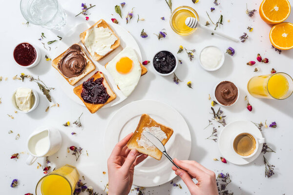 cropped view of woman spreading cream cheese on toast near drinks on white