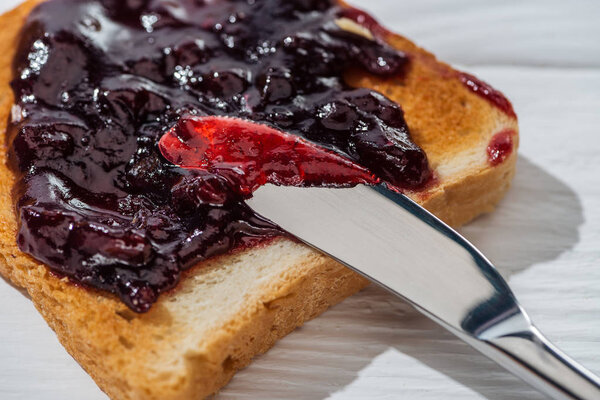 close up of toast with sweet jam near knife on white 