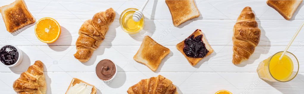 panoramic shot of sweet croissants near tasty toasts and orange juice on white 