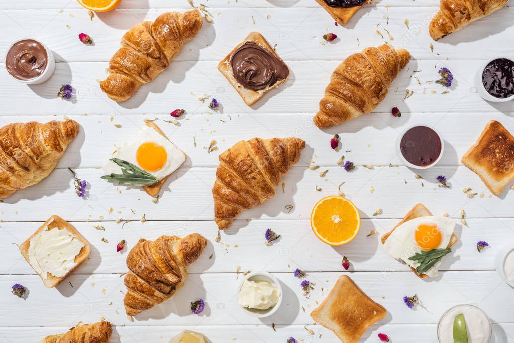 top view of sweet croissants and tasty toasts with fried eggs near dried flowers on white 