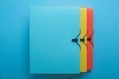 top view of multicolored paper binders in row on blue clipart