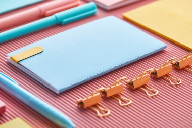 selective focus of notebook, paper clips and colorful stationery supplies on pink  clipart
