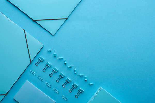 плоская укладка бумажных связующих и упорядоченных канцелярских принадлежностей, изолированных на голубом с местом для копирования
