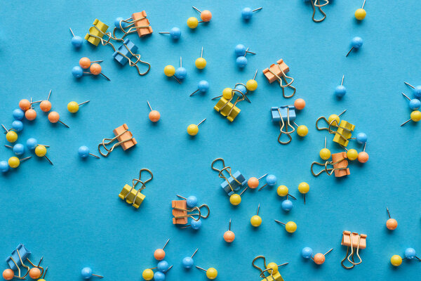 top view of colorful scattered push pins and paper clips isolated on blue