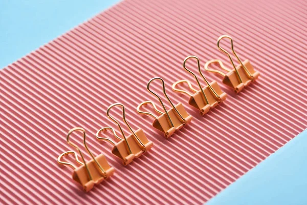 metal paper clips on textured pink paper isolated on blue