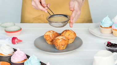 Gri üzerine izole beyaz masa üzerinde pudra şekeri ile cupcakes dekorasyon kadın kırpılmış görünümü