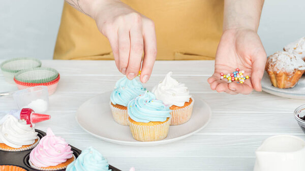 cropped view of woman decorating cupcakes with sprinkles