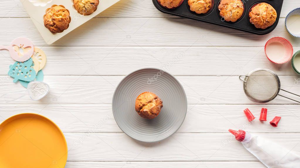 top view of delicious muffins in trays and baking tools on wooden table