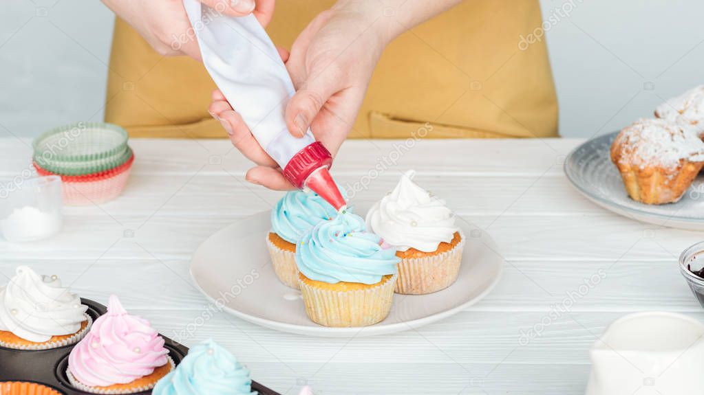 partial view of woman decorating cupcakes with icing bag