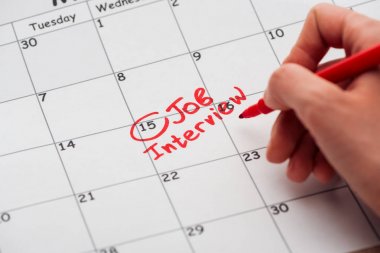 partial view of man writing with red marker on print calendar with job interview lettering clipart