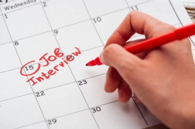 cropped view of man writing with red marker on print calendar with job interview lettering clipart