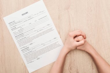 ahşap masa üzerinde özgeçmiş şablonu yakınında sıkıştırılmış elleri tutan İşveren kısmi görünümü