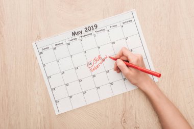 cropped view of recruiter writing with red marker on print calendar with job interview lettering clipart