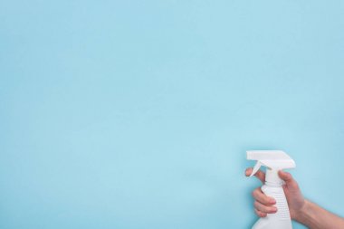 mavi arka plan üzerinde deterjan ile beyaz sprey şişesi tutan kadın kırpılmış görünümü