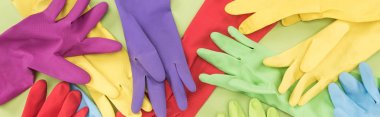 panoramic shot of messy scattered multicolored rubber gloves on green background clipart