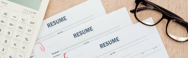 панорамный снимок стекла, калькулятора и резюме шаблонов на деревянной поверхности
