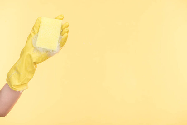 cropped view of cleaner in yellow rubber glove holding sponge with bubbles on yellow background